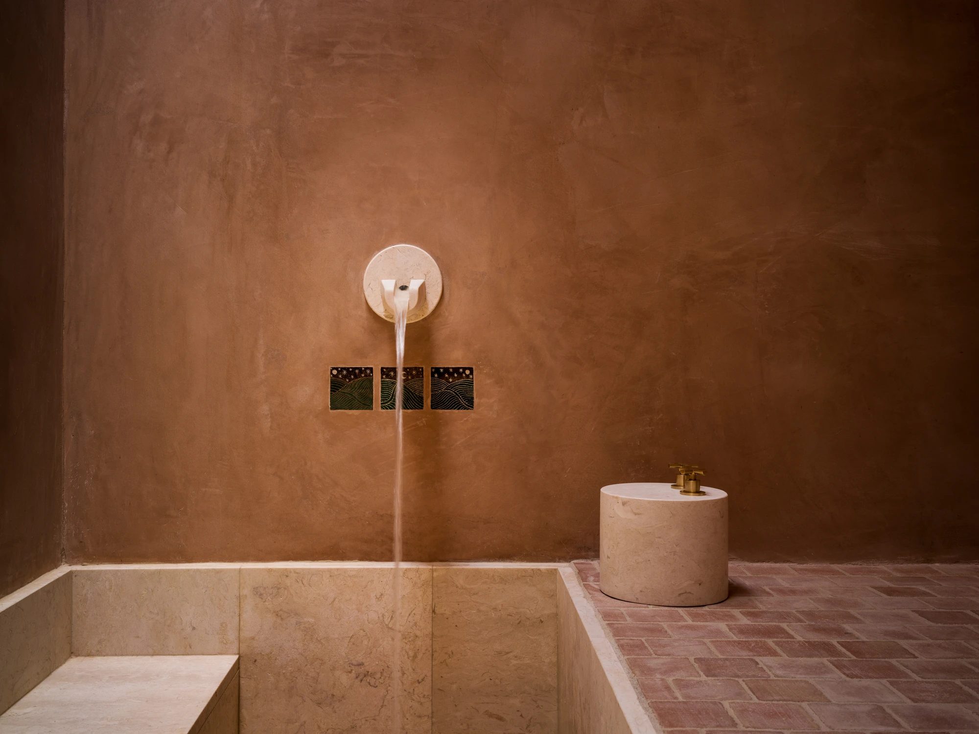 The Roman-bath spa: a sunken plunge pool cut into rammed earth, with a wall spout and a stone stool.
