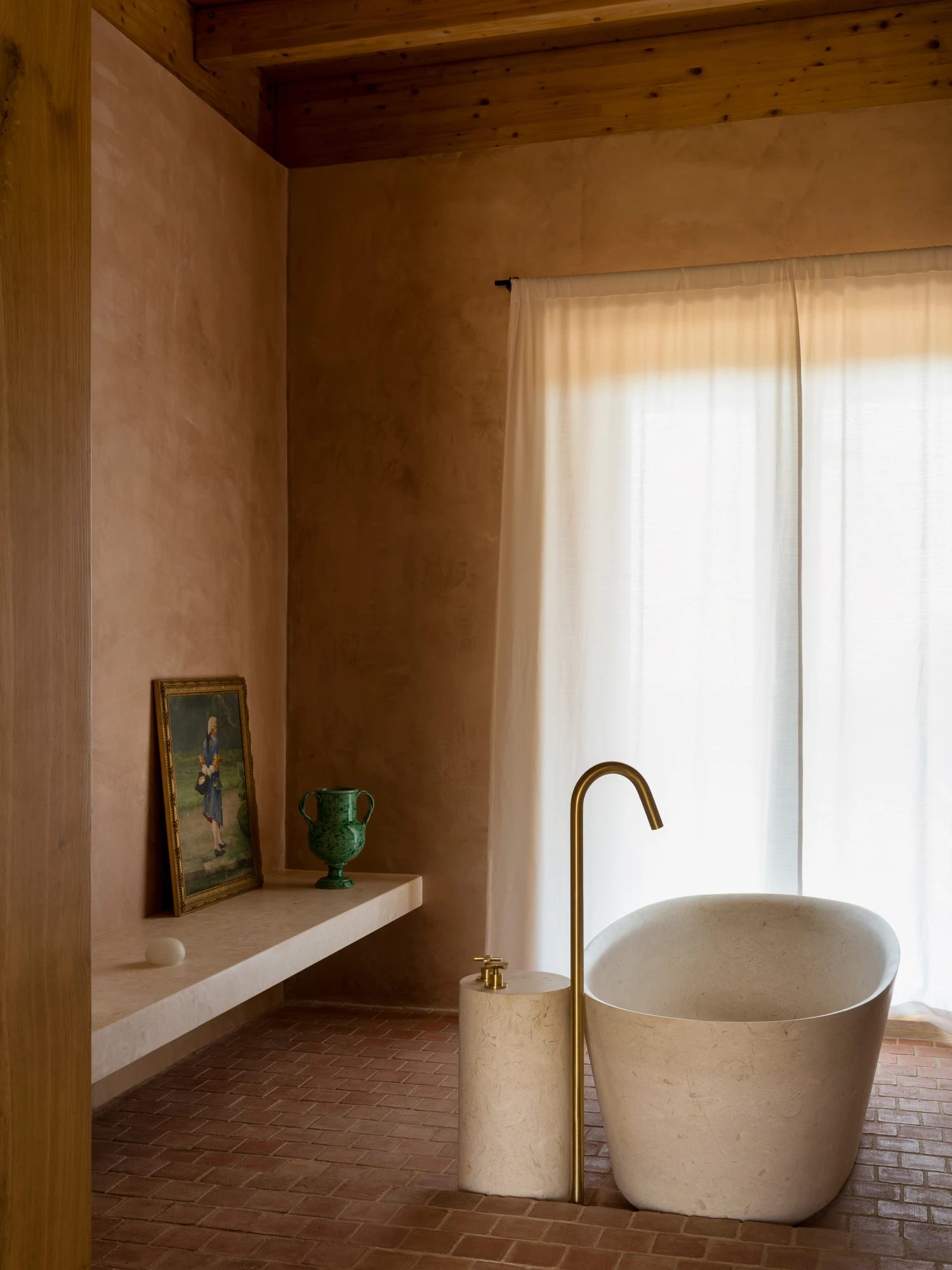 A bathroom in rammed earth, with a freestanding stone tub beside a curtained window.