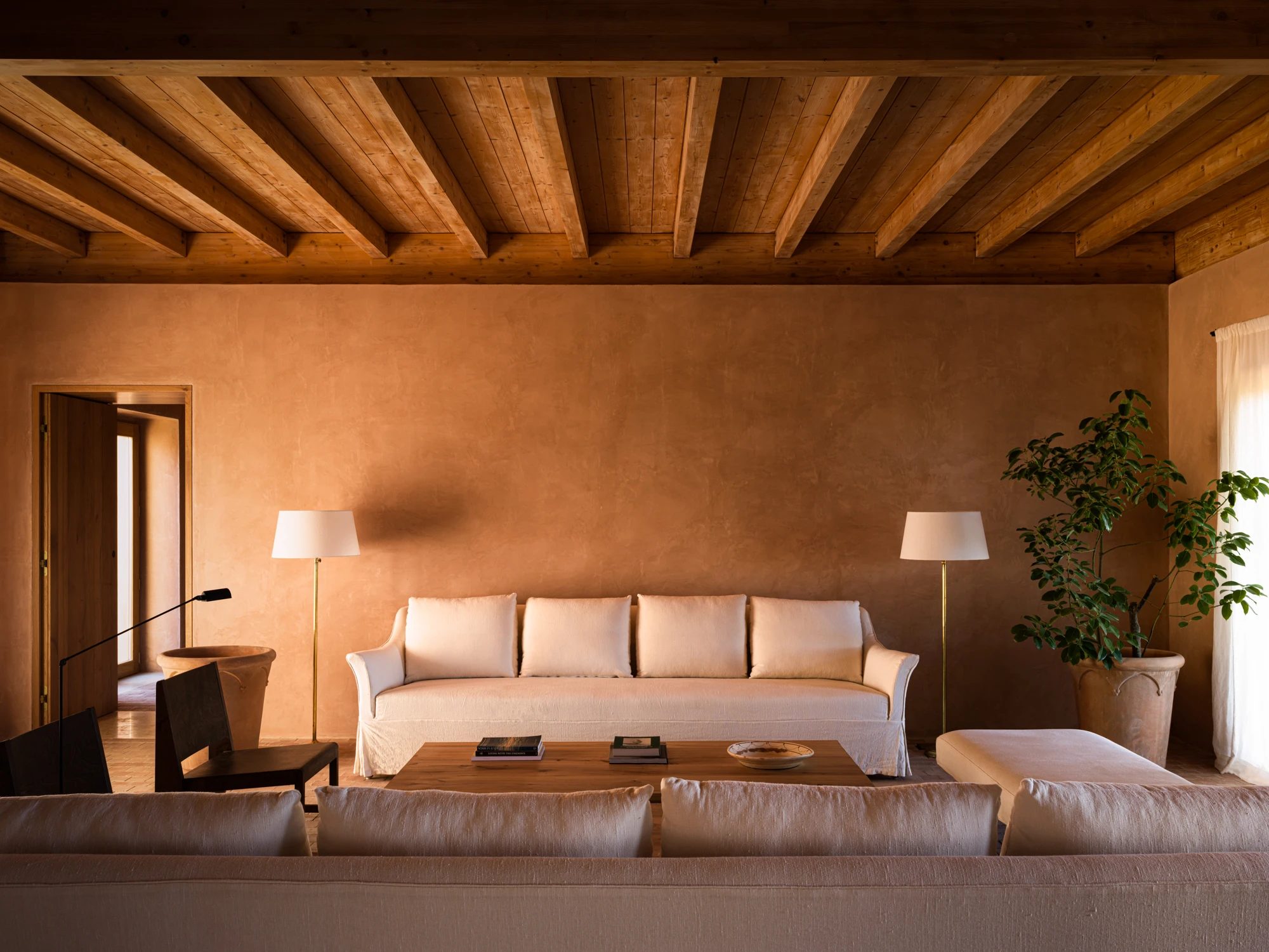 A suite under a timber-beamed ceiling, with a sofa, a low bed and a potted plant.