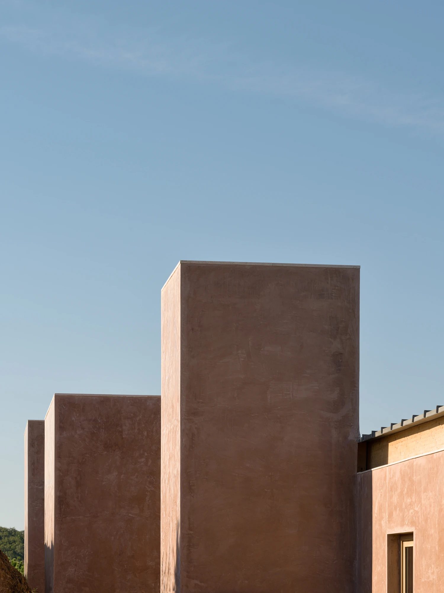 The rammed-earth volumes of the house against a clear blue sky.