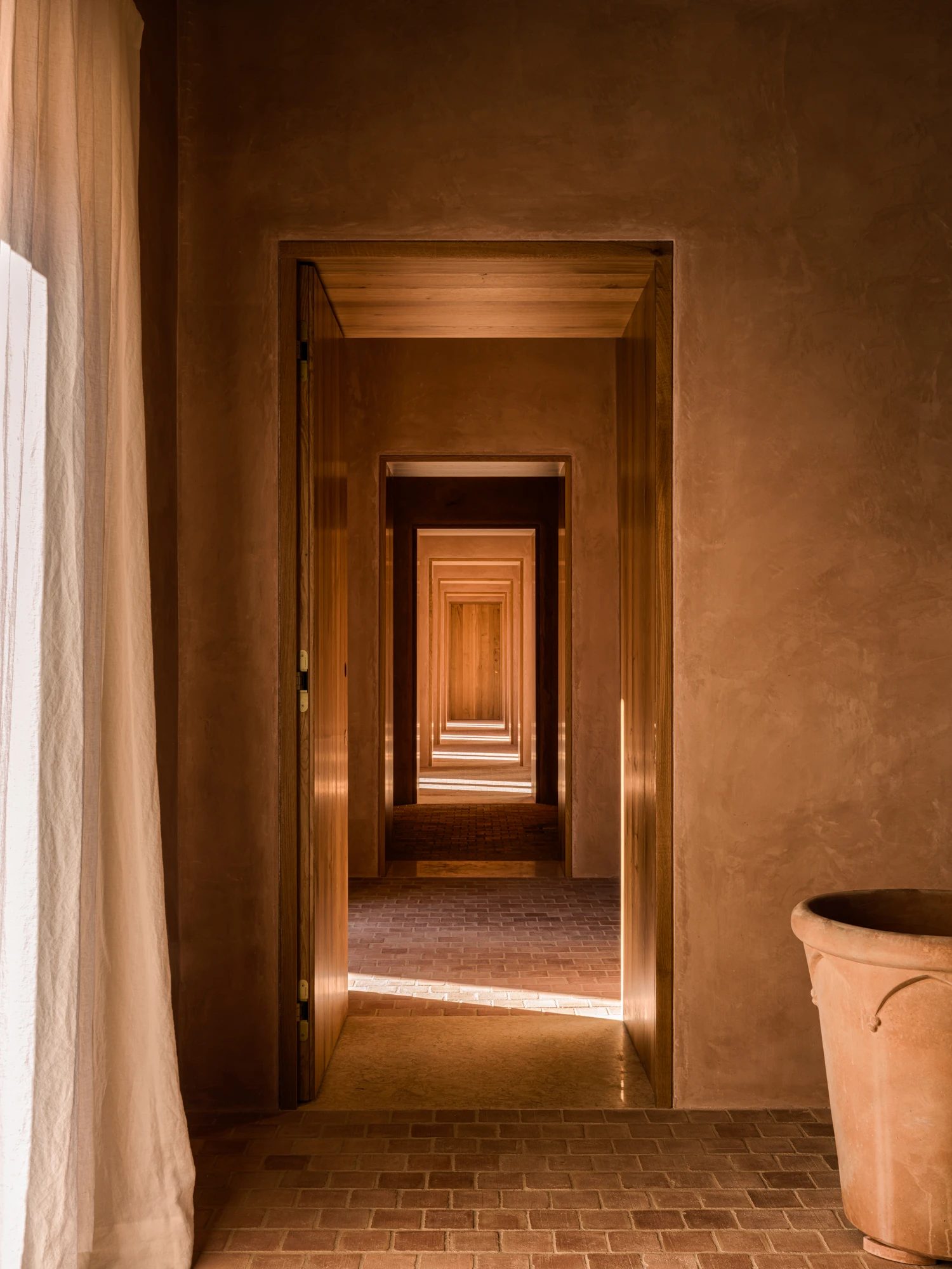 A corridor of aligned doorways, with a linen curtain and a terracotta floor.